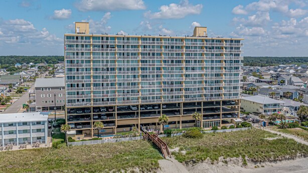 Un hôtel à plusieurs étages doté d’un parking, situé près d’une plage, avec un chemin de sable menant à l’entrée.
