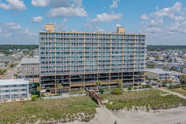 A multi-story hotel with a parking garage, located near a beach with a sandy path leading to the entrance. - Recently Updated, Wonderful Oceanfront Views + Free Attraction Tickets! (North Myrtle Beach)