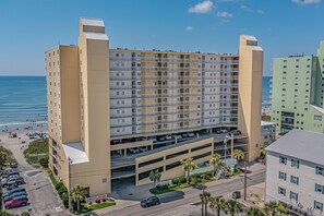 A multi-story hotel with a parking garage, located near a beach with visible ocean and beachgoers. - Recently Updated, Wonderful Oceanfront Views + Free Attraction Tickets! (North Myrtle Beach)
