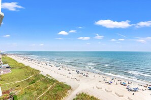Ein Strand mit einer weiten Sandfläche, einem Pier in der Ferne und einem strahlend blauen Himmel.
