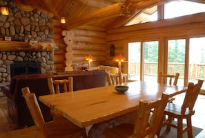 Interior de una cabaña de madera con chimenea de piedra, una mesa de comedor y una zona de estar acogedora.