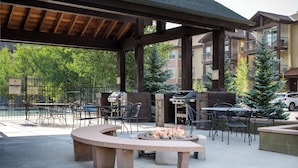 Eine Terrasse im Freien mit Feuerstelle, Grill und Gartenmöbeln.