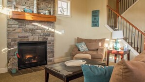 Una sala de estar con chimenea de piedra, un sofá, una mesa de centro y una escalera.