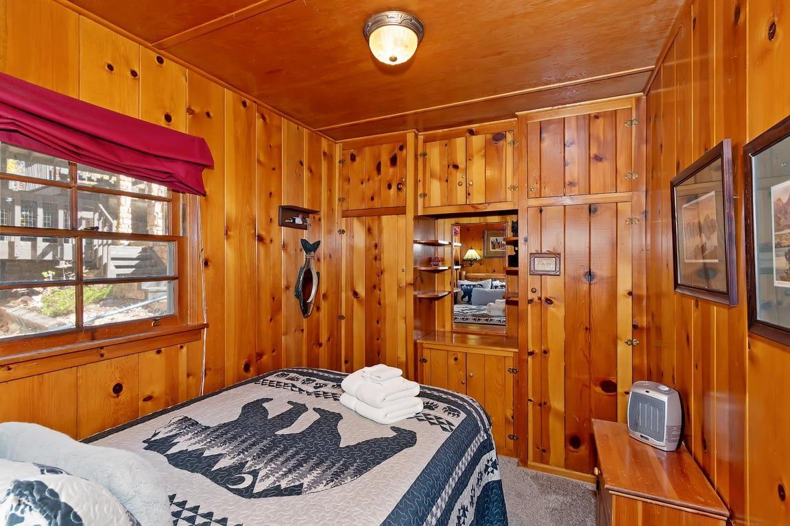 A wooden-paneled room with a bed, a television, and a window with a red curtain.