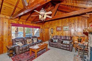 A cozy cabin interior with two leather sofas, a wooden coffee table, and a ceiling fan.