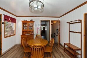 A dining area with a wooden table and chairs, a cabinet with dishes, and a coat rack.