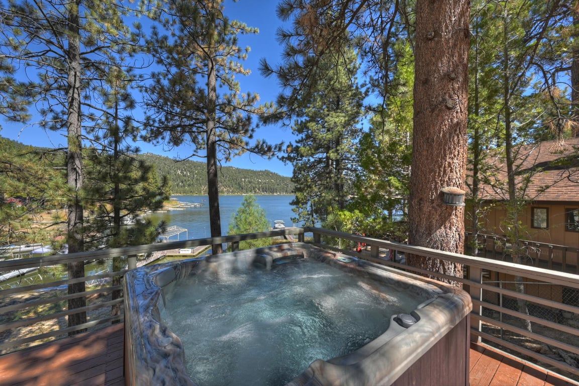 A hot tub on a wooden deck with a lake view, surrounded by trees.