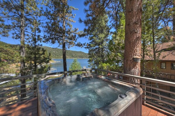 A hot tub on a wooden deck with a lake view, surrounded by trees.