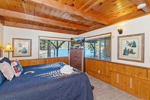 A bedroom with a bed, wooden ceiling, windows, a dresser, and framed pictures on the wall.
