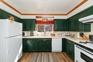 A kitchen with green cabinets, a white refrigerator, a microwave, a dishwasher, and a stove.