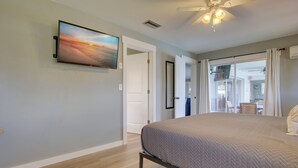 Une chambre avec un lit, un ventilateur de plafond, un téléviseur fixé au mur et une vue sur l’extérieur, visible à travers une porte vitrée.