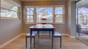 Une pièce avec une table et un banc en bois, de grandes fenêtres et un lustre.
