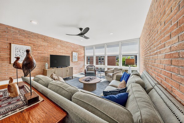A spacious living room with a brick wall, a large window, and a ceiling fan.