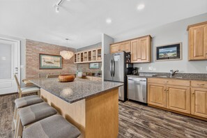A modern kitchen with a central island, wooden cabinets, and a brick accent wall.