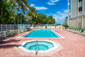 Une piscine avec un jacuzzi, entourée de chaises longues et d’une clôture.