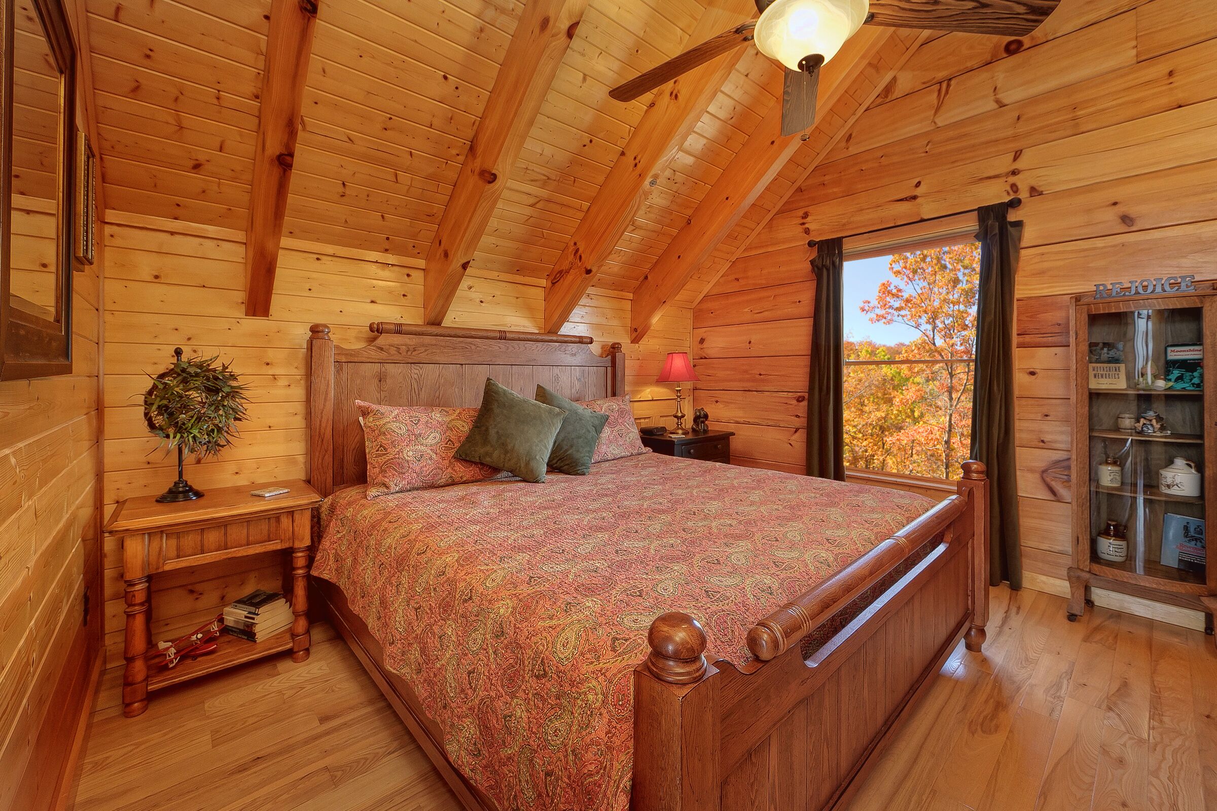 A wooden cabin bedroom with a bed, nightstands, a lamp, and a cabinet with glass doors.