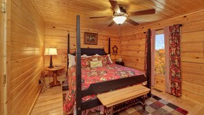 Un dormitorio de cabaña de madera con cama con dosel, ventilador de techo, mesita de noche y ventana con cortinas.