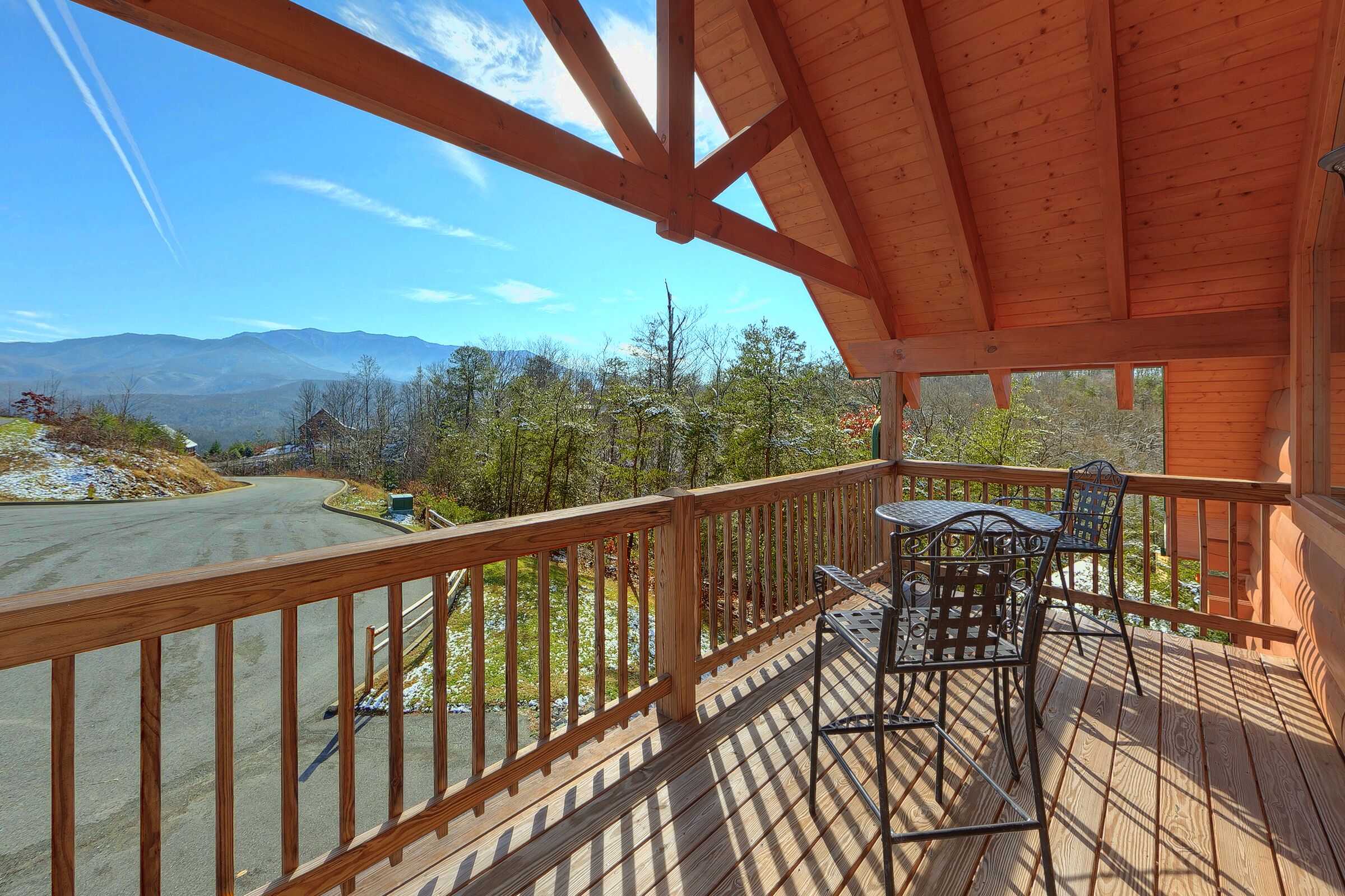 Une terrasse en bois avec une table et des chaises, d’où l’on a vue sur une route et des montagnes.