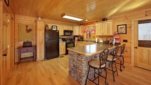 Cocina de cabaña de madera con una isla central, taburetes de bar, refrigerador, estufa, microondas y armarios de madera.