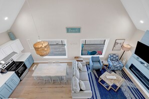 A modern kitchen with white cabinets and a dining area with a white table and chairs. There is a sofa and a patterned armchair in the living area.