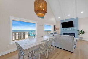 Un comedor con vistas al océano, una sala de estar con chimenea y un televisor montado en la pared.