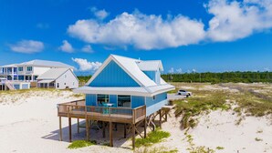 A beach house with a balcony, a car, and a sandy beach. - Gulf Front | Pet Friendly | Shared Heated Pool (Gulf Shores)