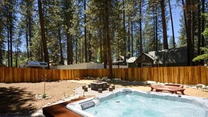 A hot tub in a backyard with a wooden fence, surrounded by trees and a house.