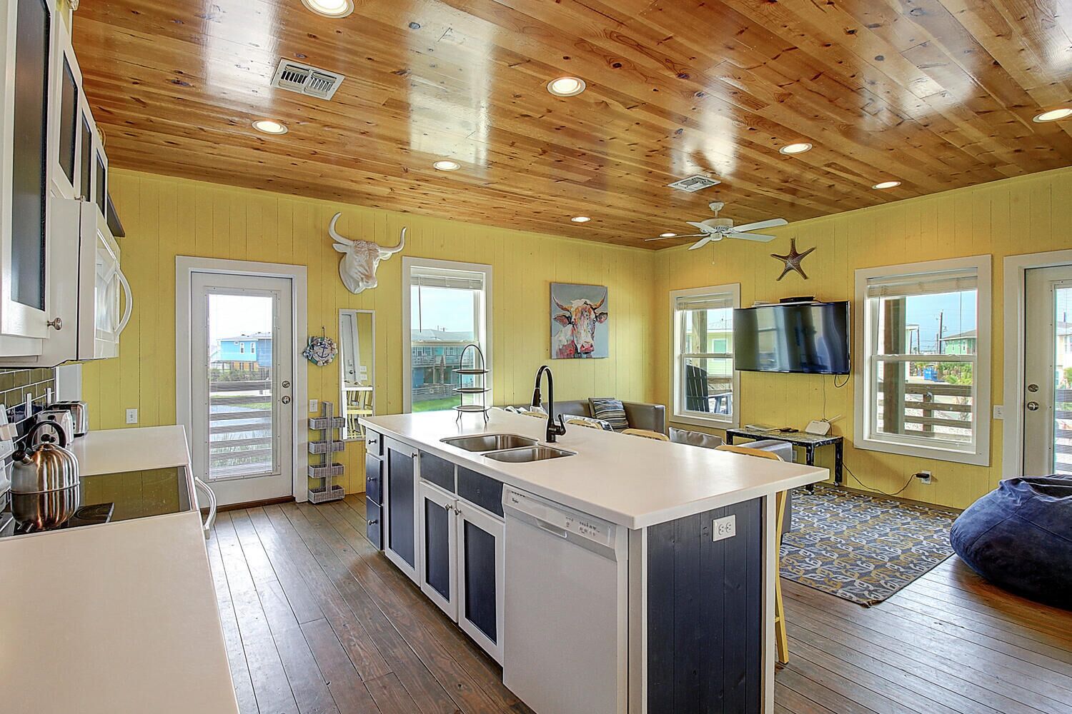 A spacious kitchen with a central island, wooden ceiling, and large windows offering views of the outside.