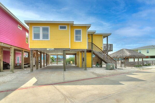 A yellow building with a covered outdoor area, wooden deck, and a thatched-roof structure.