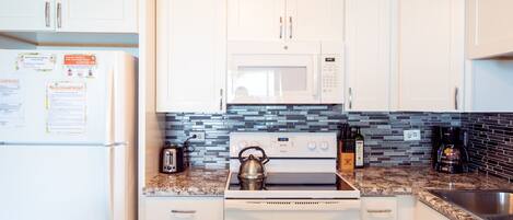 A kitchen with white cabinets, a microwave, a stove, a toaster, and a coffee maker.