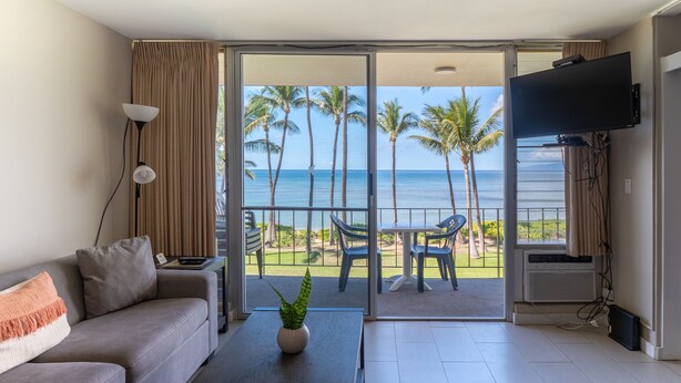 A modern hotel room with a balcony, a sofa, a coffee table, and a TV. - Oceanfront, walk to shops and restaurants (Kihei)