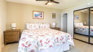 A bedroom with a bed, nightstands, a ceiling fan, and a large mirror. - Oceanfront, walk to shops and restaurants (Kihei)