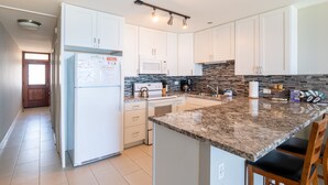 A modern kitchen with white cabinets, a granite countertop, and a built-in oven. - Oceanfront, walk to shops and restaurants (Kihei)