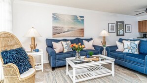 A living room with two blue sofas, a white coffee table, wicker chairs, and a beach-themed wall art. - 🌴Welcome to The Islander Unit #203 Your Perfect Destin Beach Escape🌅 (Destin)