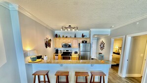 Une cuisine moderne dotée d’un îlot central, de tabourets de bar, d’un plancher en bois et donnant sur une chambre.