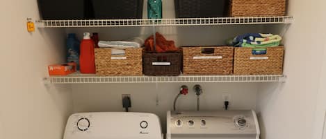 A laundry room with two front-loading washing machines and three shelves above containing baskets and storage boxes.