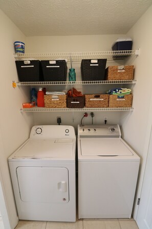 A laundry room with two front-loading washing machines and three shelves above containing baskets and storage boxes.
