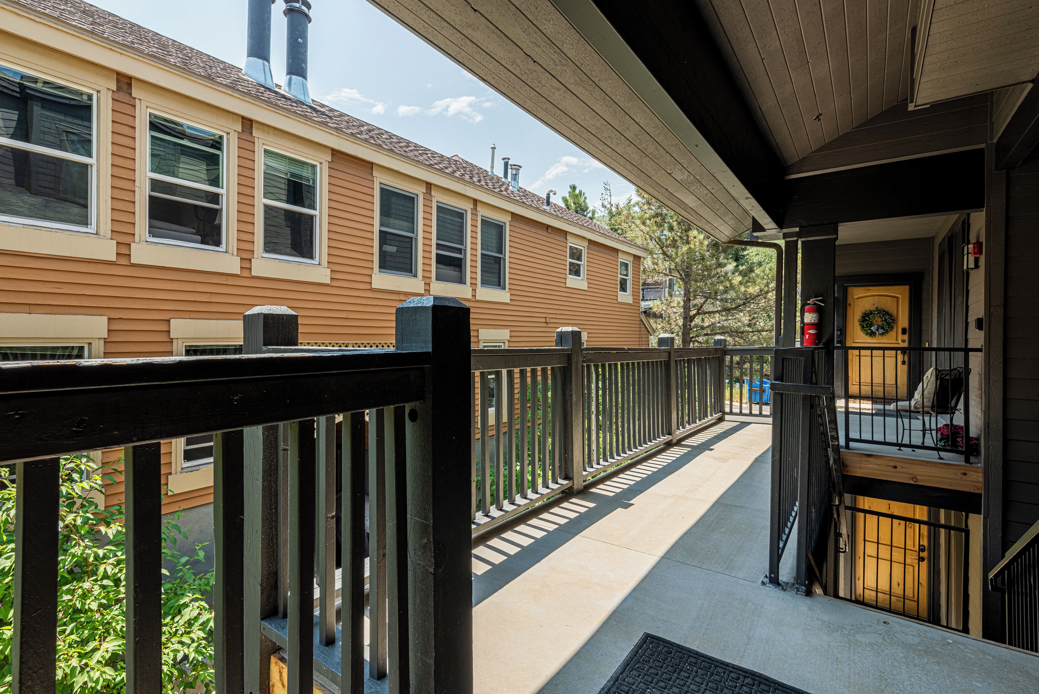 A wooden house with a balcony, a fire extinguisher, and a door with a wreath.