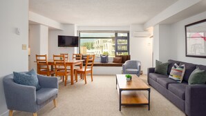A modern living room with a dining area, a sofa, a coffee table, and a TV mounted on the wall. - 1BR | Carleton Lodge | Unbeatable Mountain Base Location | Ski in / out | | Free Parking (Whistler)