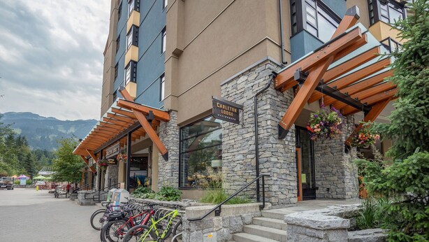 A multi-story building with a stone facade and wooden beams, labeled "Carleton Lodge". - 1BR | Carleton Lodge | Unbeatable Mountain Base Location | Ski in / out | | Free Parking (Whistler)