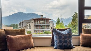 A view from a window with a cushioned bench, a building labeled "The Crystal," and mountains in the background. - 1BR | Carleton Lodge | Unbeatable Mountain Base Location | Ski in / out | | Free Parking (Whistler)