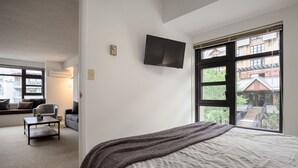 A bedroom with a large bed, a TV mounted on the wall, and a window with a view of buildings and greenery. - 1BR | Carleton Lodge | Unbeatable Mountain Base Location | Ski in / out | | Free Parking (Whistler)