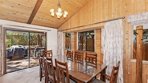 A wooden interior with a dining table and chairs, large windows, and a ceiling fan. - Fox Canyon by Destination Big Bear : Hot Tub! BBQ! Air Hockey! Internet! Deck! Great Neighborhood! Fireplace! (Big Bear Lake)