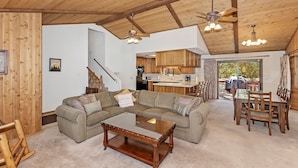 A spacious living area with a wooden ceiling, a sectional sofa, a glass coffee table, and a dining area with wooden chairs. - Fox Canyon by Destination Big Bear : Hot Tub! BBQ! Air Hockey! Internet! Deck! Great Neighborhood! Fireplace! (Big Bear Lake)
