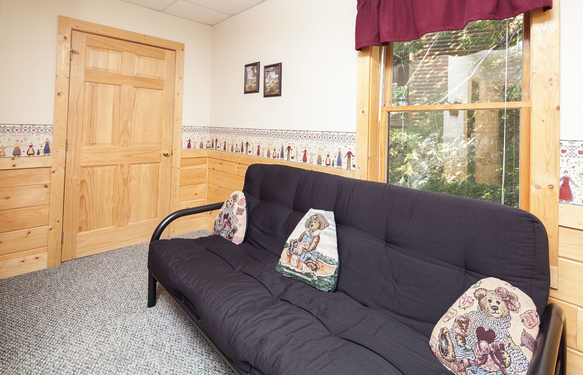 Een kamer met een zwarte bank, twee decoratieve kussens, een houten deur, een raam met uitzicht en een betegelde rand aan de muur.