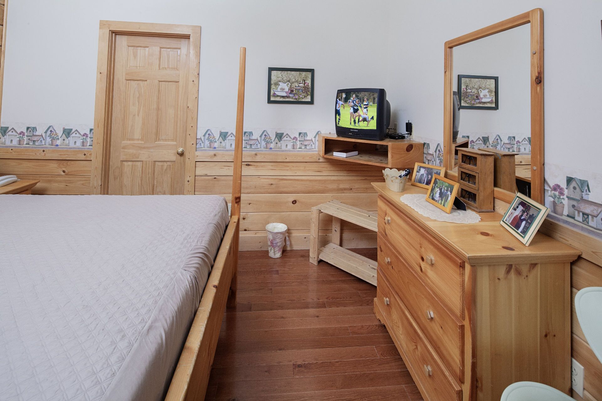 Habitación de madera con cama, cómoda y televisor.