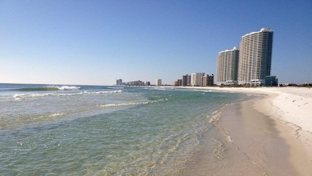 Una playa con agua cristalina, una orilla arenosa y edificios altos al fondo.