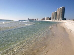 A beach with clear water, sandy shore, and high-rise buildings in the background.
