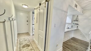 Un pasillo con un rug adornado, una puerta blanca y un área de lavandería con lavadoras apiladas.