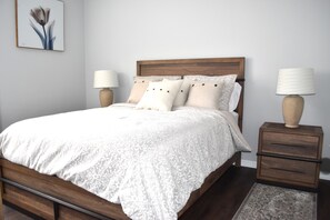 A neatly made bed with a wooden headboard, two bedside tables with lamps, and a framed artwork on the wall.